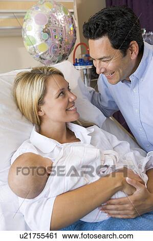 Stock Image - New mother with baby and husband in hospital smiling. Fotosearch