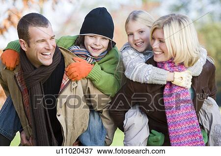 Stock Photo - Parents outdoors piggybacking two young children and smiling (selective focus). Fotosearch