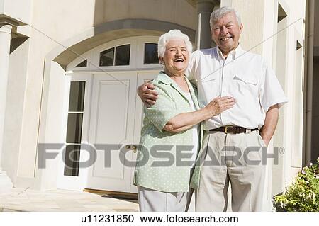 Stock Image - Senior couple standing outside their home. Fotosearch