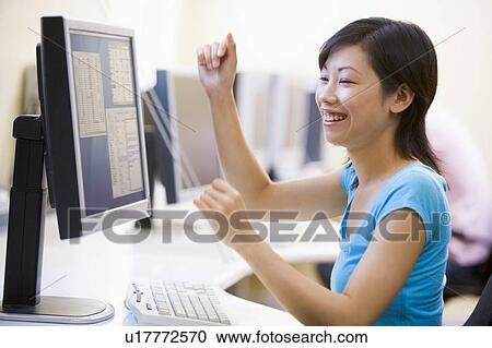 Stock Image - Woman in computer room cheering and smiling. Fotosearch