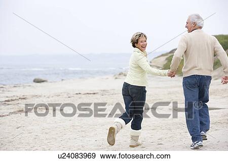 Stock Photo - Couple at the beach holding hands and smiling. Fotosearch