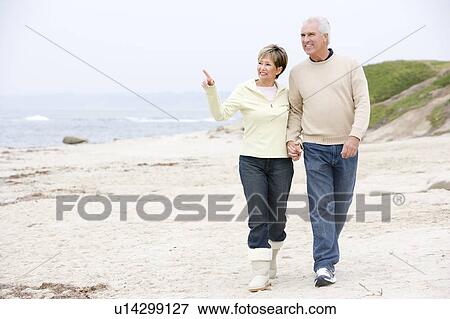 Couple holding hands at the beach smiling and pointing View Large Photo Image Stock Photo - Couple holding hands at the beach smiling and pointing. Fotosearch