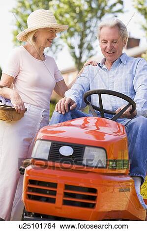 Picture - Couple outdoors with tools and lawnmower smiling. Fotosearch