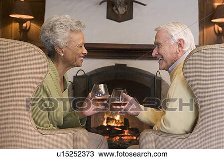 Couple sitting in living room by fireplace with drinks smiling View Large Photo Image Stock Image - Couple sitting in living room by fireplace with drinks smiling. Fotosearch