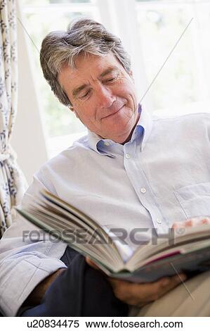 Stock Photography - Man in living room reading book smiling. Fotosearch
