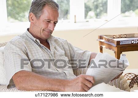 Stock Photograph - Man in living room reading newspaper smiling. Fotosearch