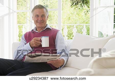 Man in living room with coffee reading newspaper smiling View Large Photo Image Stock Photo - Man in living room with coffee reading newspaper smiling. Fotosearch