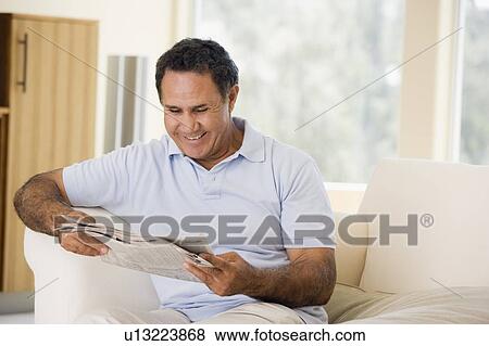 Stock Photo - Man relaxing with newspaper in living room and smiling. Fotosearch
