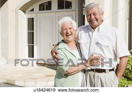 Stock Photo - Senior couple standing outside their home. Fotosearch