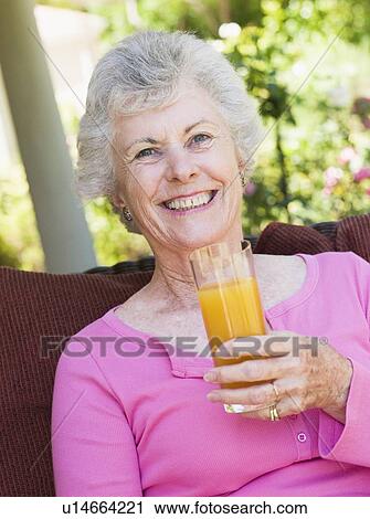Senior woman sitting outdoors with a glass of orange juice View Large Photo Image Stock Image - Senior woman sitting outdoors with a glass of orange juice. Fotosearch