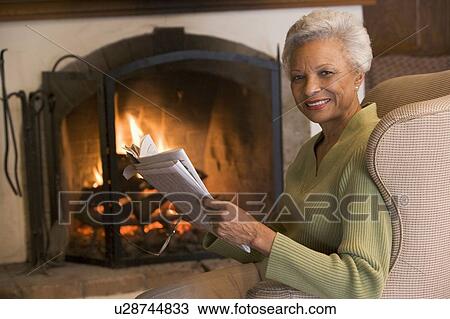 Woman sitting in living room by fireplace with newspaper smiling View Large Photo Image Stock Image - Woman sitting in living room by fireplace with newspaper smiling. Fotosearch