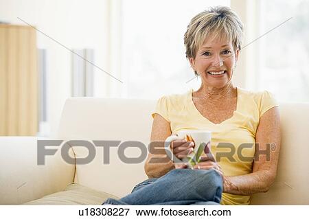 Stock Photo - Woman sitting in living room with coffee smiling. Fotosearch