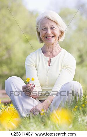 Woman sitting outdoors smiling and holding a Buttercup flower View Large Photo Image Stock Photo - Woman sitting outdoors smiling and holding a Buttercup flower. Fotosearch
