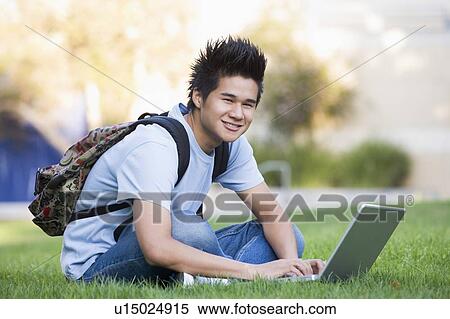 Stock Photography - Man outdoors sitting on grass with laptop (selective focus). Fotosearch