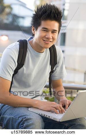 Stock Photography - Man sitting on bench outdoors using laptop (selective focus). Fotosearch