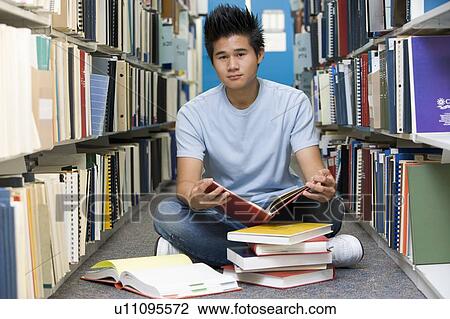 Stock Image - Man sitting on floor in library holding book. Fotosearch
