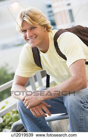 Stock Photo - Man sitting outdoors on bench smiling (selective focus). Fotosearch