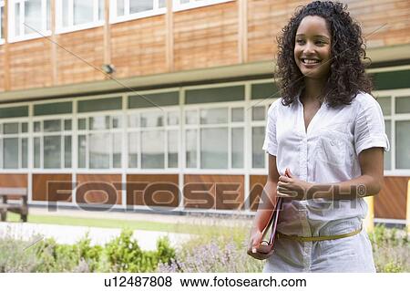 Stock Photo - Student standing outdoors smiling and holding binder. Fotosearch