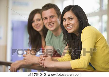 Stock Image - Three people in corridor leaning on railing (depth of field). Fotosearch