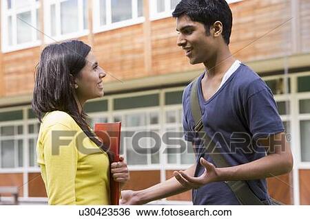 Two students standing outdoors smiling and talking View Large Photo Image Stock Photograph - Two students standing outdoors smiling and talking. Fotosearch