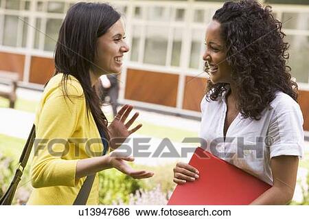 Two students standing outdoors talking View Large Photo Image Stock Photograph - Two students standing outdoors talking. Fotosearch