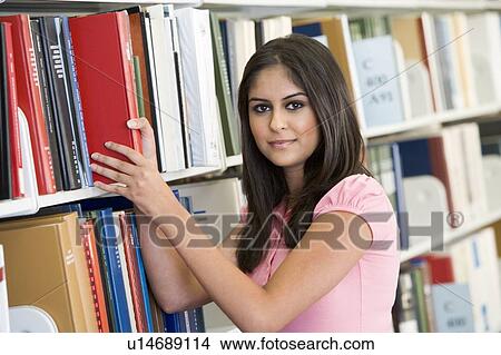 Picture - Woman in library pulling book off a shelf (depth of field). Fotosearch