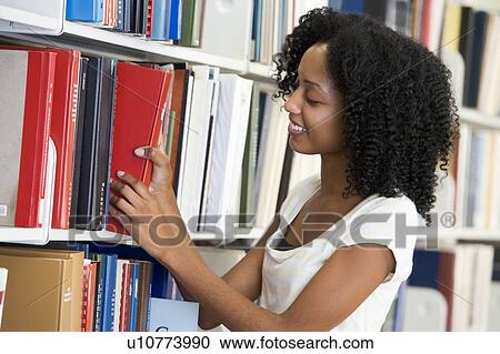 Stock Image - Woman in library pulling book off a shelf (depth of field). Fotosearch