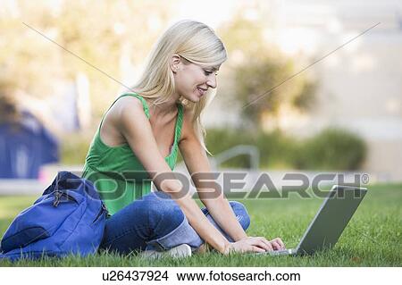 Picture - Woman outdoors sitting on grass with laptop (selective focus). Fotosearch