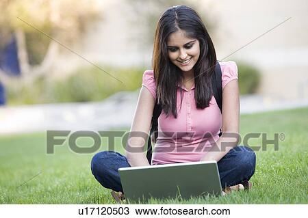 Stock Image - Woman outdoors sitting on grass with laptop (selective focus). Fotosearch