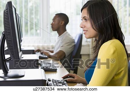 Woman sitting at a computer terminal with man in background (selective focus/high key) View Large Photo Image Picture - Woman sitting at a computer terminal with man in background (selective focus/high key). Fotosearch