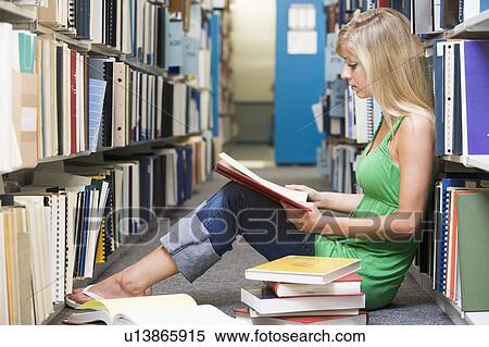 Stock Photography - Woman sitting on floor in library reading book. Fotosearch