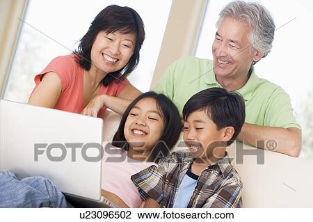 Stock Image - Couple with two young children in living room with laptop smiling. Fotosearch