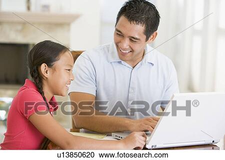 Stock Image - Man and young girl with laptop in dining room smiling. Fotosearch