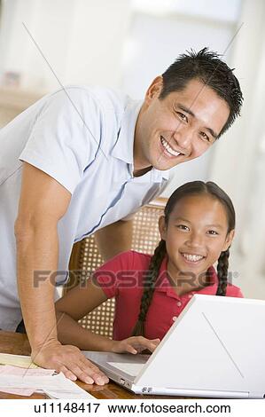 Stock Photo - Man and young girl with laptop in dining room smiling. Fotosearch