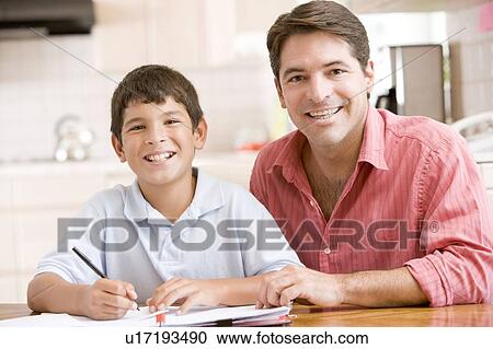 Stock Image - Man helping young boy in kitchen doing homework and smiling. Fotosearch