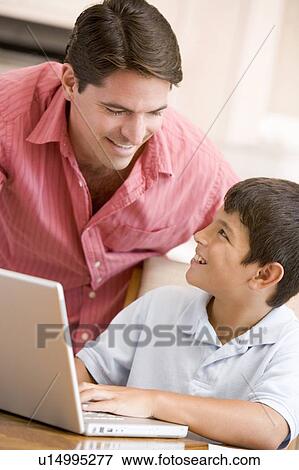 Stock Photo - Man helping young boy in kitchen with laptop smiling. Fotosearch