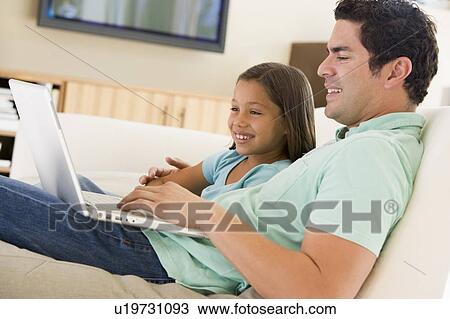 Stock Image - Man with young girl in living room with laptop smiling. Fotosearch