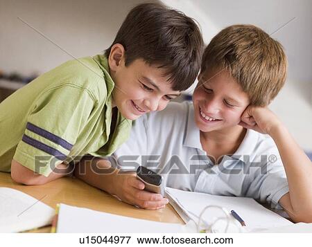 Stock Photo - Two Young Boys Distracted From Their Homework, Playing With A Cellphone. Fotosearch