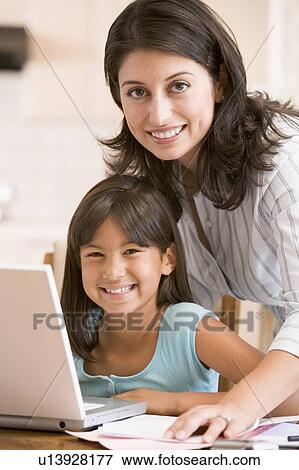 Stock Photo - Woman and young girl in kitchen with laptop and paperwork smiling. Fotosearch