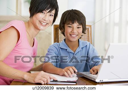 Woman helping young boy with laptop do homework in dining room smiling View Large Photo Image Stock Photo - Woman helping young boy with laptop do homework in dining room smiling. Fotosearch