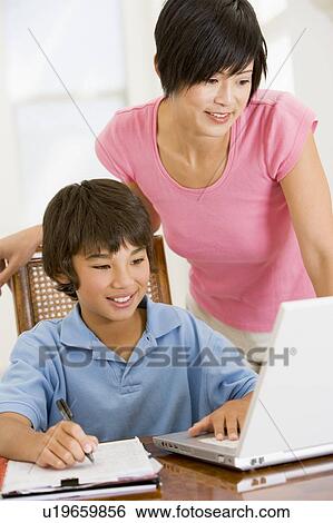 Woman helping young boy with laptop do homework in dining room smiling View Large Photo Image Stock Photograph - Woman helping young boy with laptop do homework in dining room smiling. Fotosearch