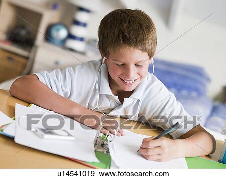 Stock Photo - Young Boy Doing His Homework While Listening To Music On His MP3 Player. Fotosearch