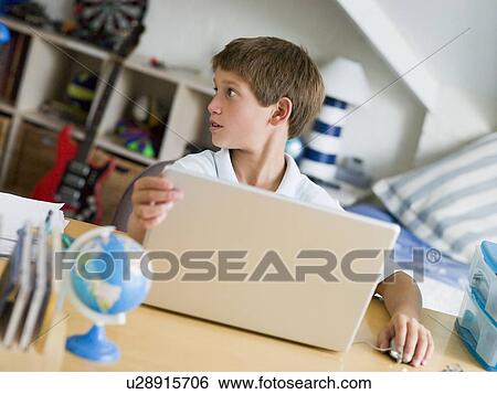 Stock Photograph - Young Boy Using A Laptop In His Bedroom. Fotosearch