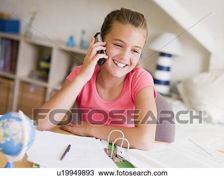 Stock Image - Young Girl Distracted From Her Homework, Talking On A Cellphone. Fotosearch