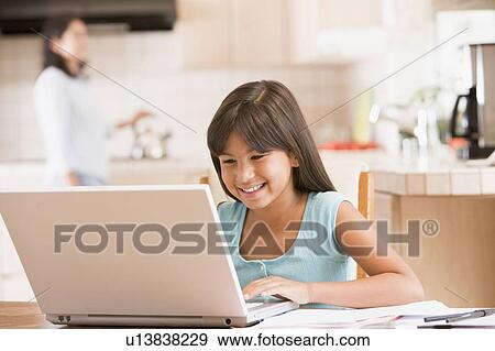 Stock Photo - Young girl in kitchen with laptop and paperwork smiling with woman in background. Fotosearch