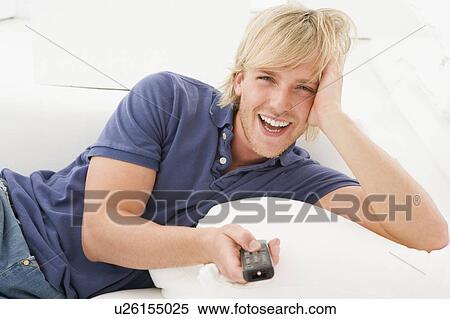 Man in living room holding remote control laughing View Large Photo Image Stock Photography - Man in living room holding remote control laughing. Fotosearch