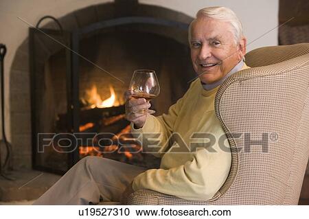 Stock Image - Man in living room with drink smiling. Fotosearch