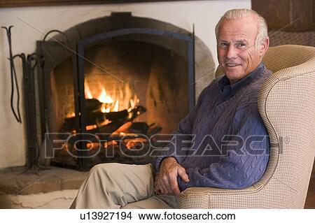 Picture - Man sitting in living room by fireplace smiling. Fotosearch