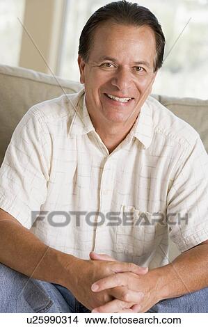 Picture - Man sitting in living room smiling. Fotosearch