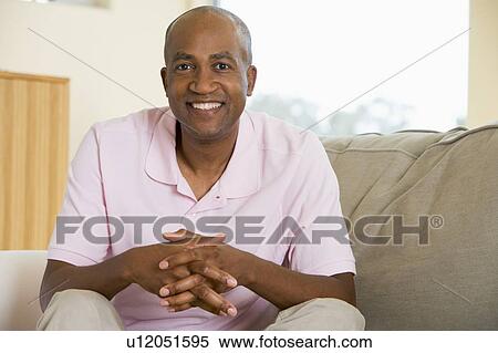 Stock Photography - Man sitting in living room smiling. Fotosearch